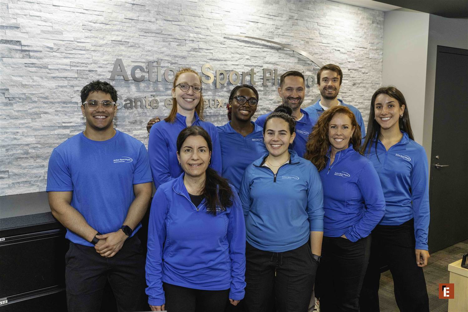 A clinic team in front of the Action Sport Physio wall